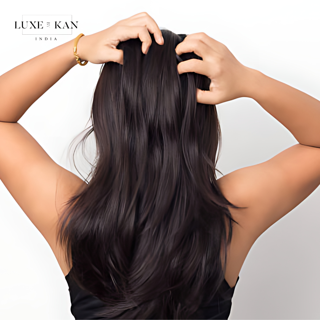 A woman with long, dark hair runs her fingers through it, showcasing its shine and softness against a plain white background.