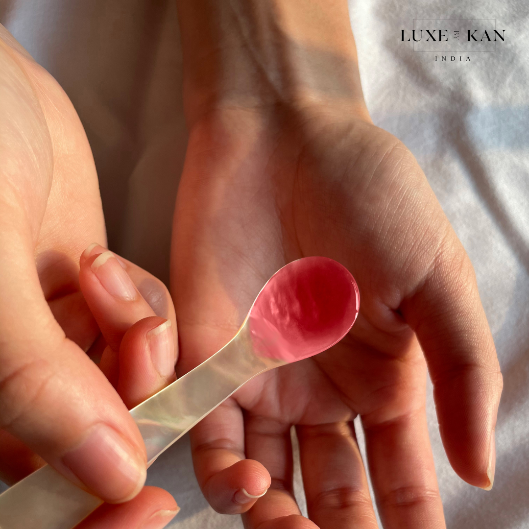 A hand holding a spoon with glossy pink substance, positioned over an open palm, on a softly.