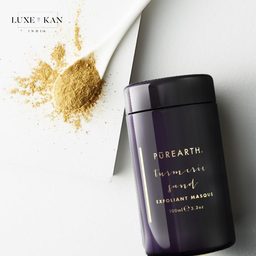 A dark container of Purearth Turmeric Sand Exfoliant Masque next to a spoonful of golden turmeric powder on a light background.