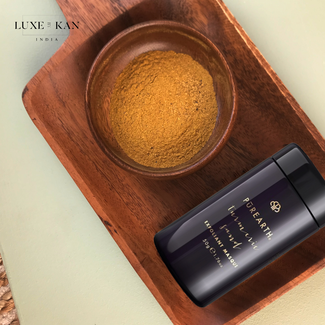 A wooden bowl holds golden powder next to a sleek black container of Purearth Exfoliating Masque on a textured surface.