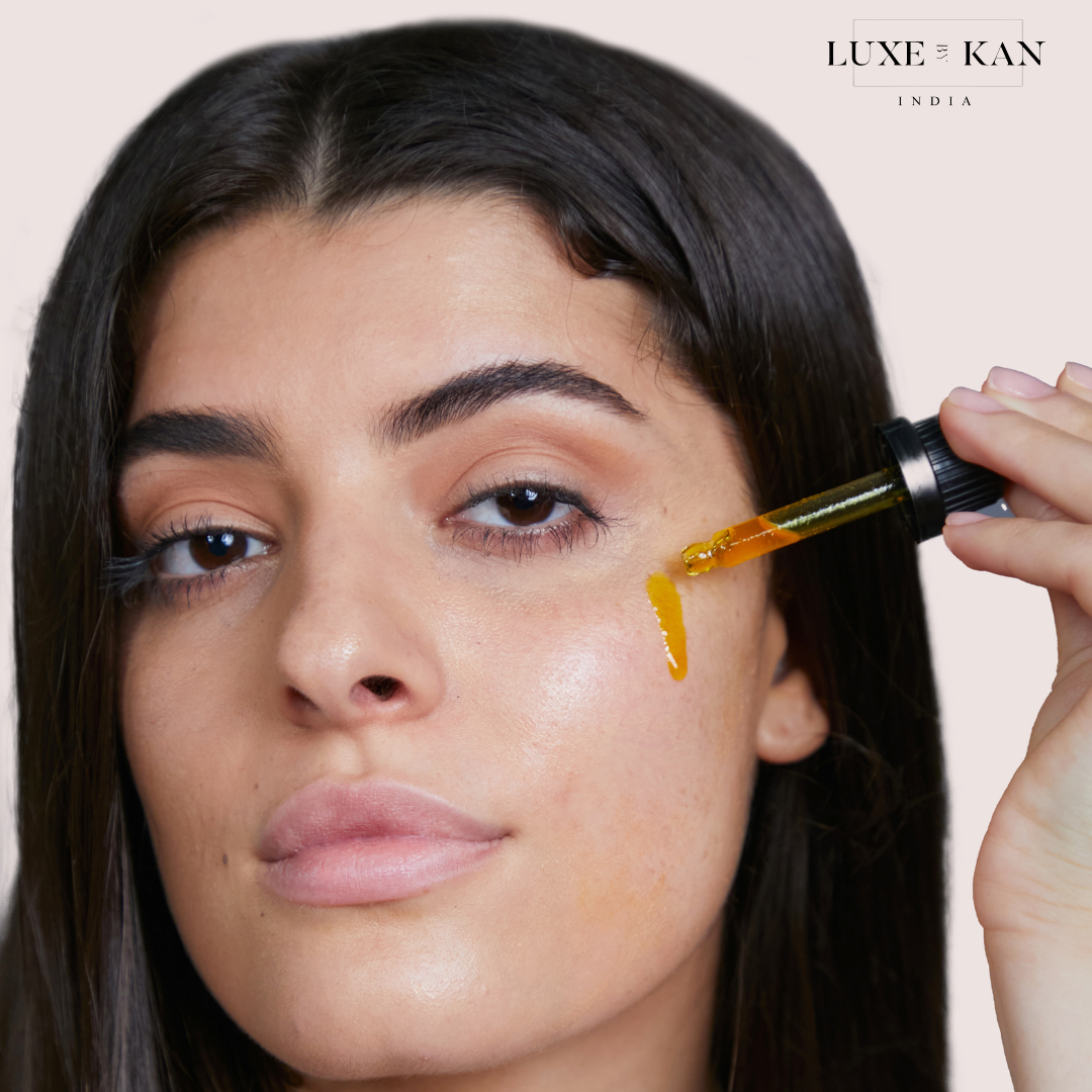 A person applies a dropper of facial oil to their skin, showcasing the product from Luxe Kan against a soft background.