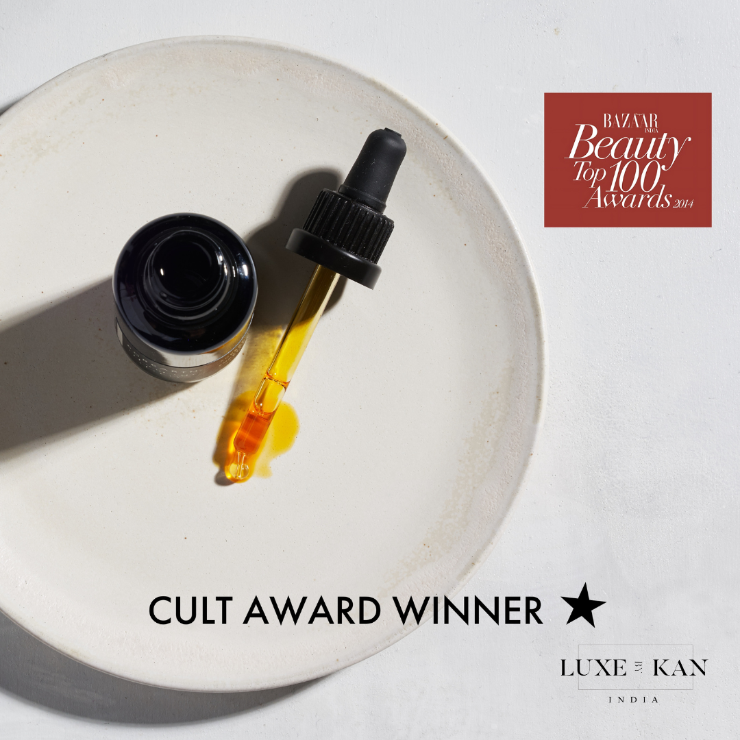 A dropper bottle with yellow oil sits on a white plate, showcasing its "Cult Award Winner" label and "Beauty Top 100 Awards 2014" recognition.