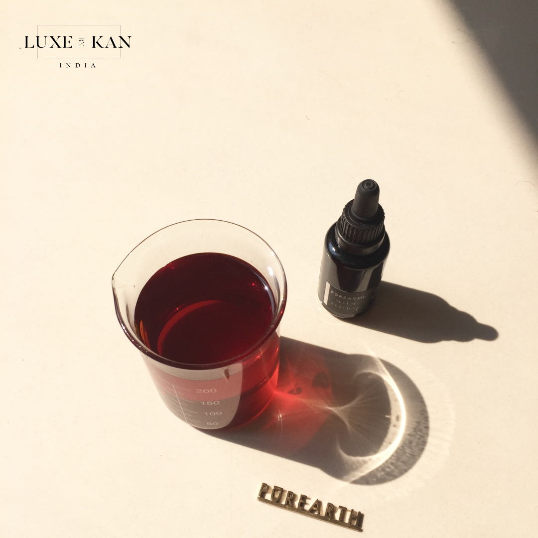 Glass filled with red liquid sits beside a dropper bottle of serum and a golden "POREARTH" label on a light surface.