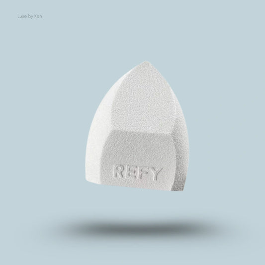 Close-up of a light gray Refy beauty sponge, displaying a textured surface and the brand name.