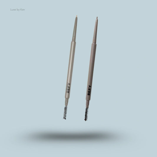 Two Refy double-ended brow pencils with slim retractable tips and spoolie brushes, suspended in mid-air.