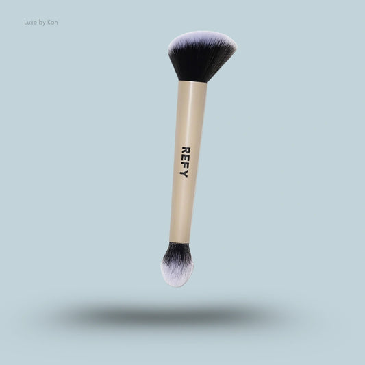 Refy double-ended face brush with black bristles, white tips, and a beige handle with black lettering.