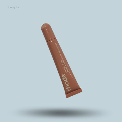 A tube of Rhode Peptide Lip Tint Balm in a toast shade, showing the product name on a light blue background.