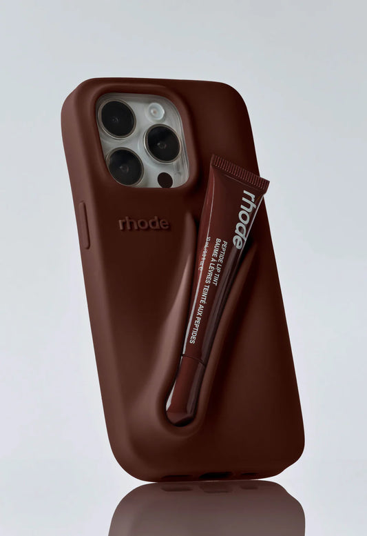 Chocolate-brown Rhode fall lip phone case with matching Peptide Lip Tint secured in the case's designed groove.