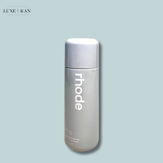 A sleek, gray glazing milk skincare bottle labeled "rhode" with a silver cap, featuring facial essence branding.