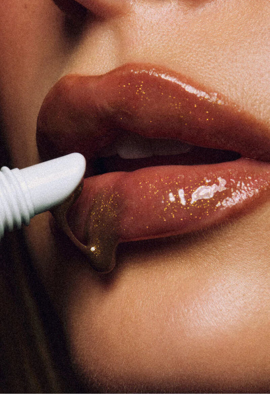 Close-up shot of lips with Rhode Peptide Lip Treatment Cinnamon Roll being applied. The lips are glossy with gold glitter detailing.