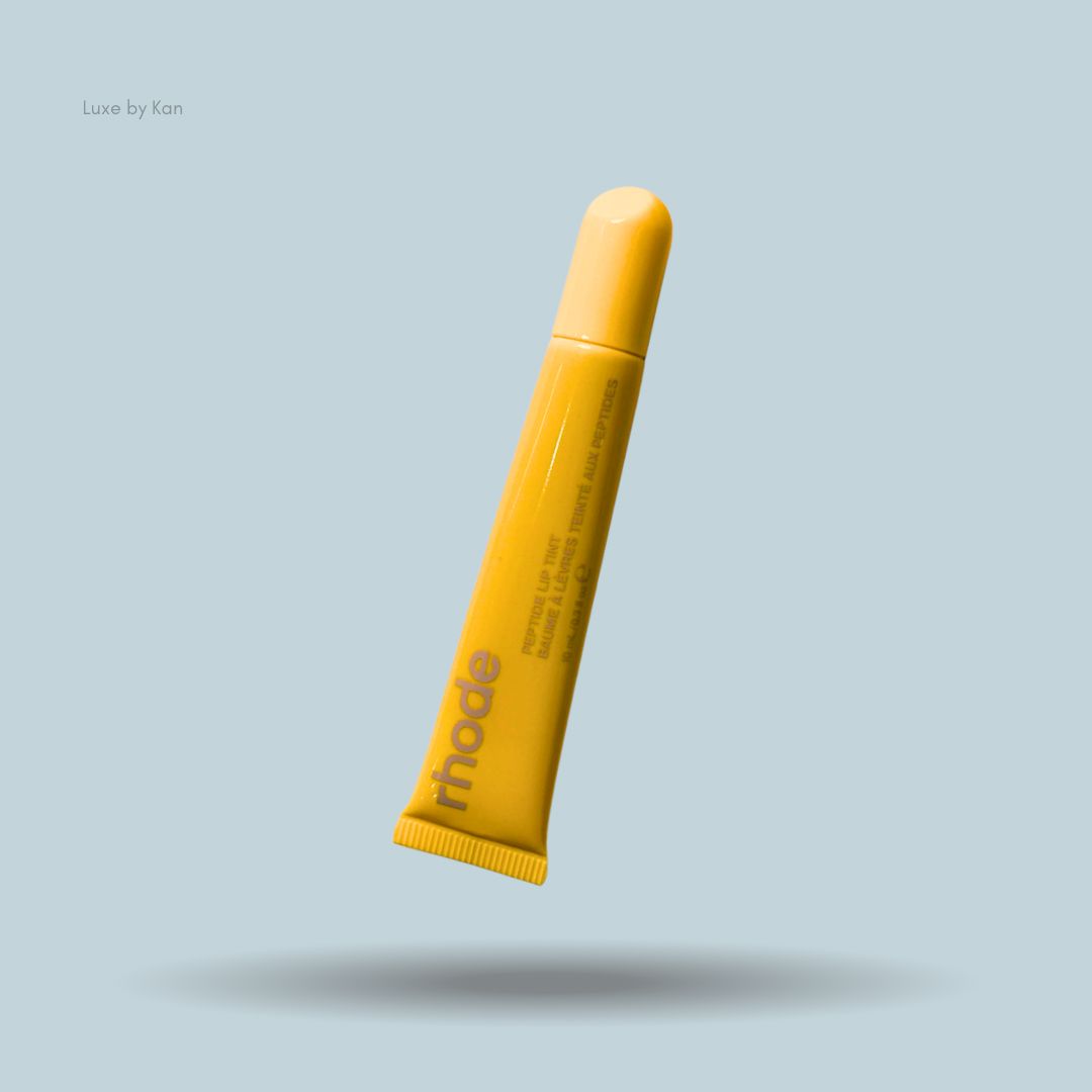 A yellow tube of Rhode Peptide Lip Tint floating at an angle over a soft shadow on a light blue-grey background.