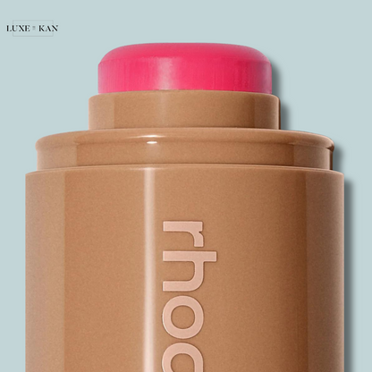 Close-up of a creamy bronzer stick in a warm brown shade, topped with vibrant pink. The brand name "rhood" is subtly displayed.
