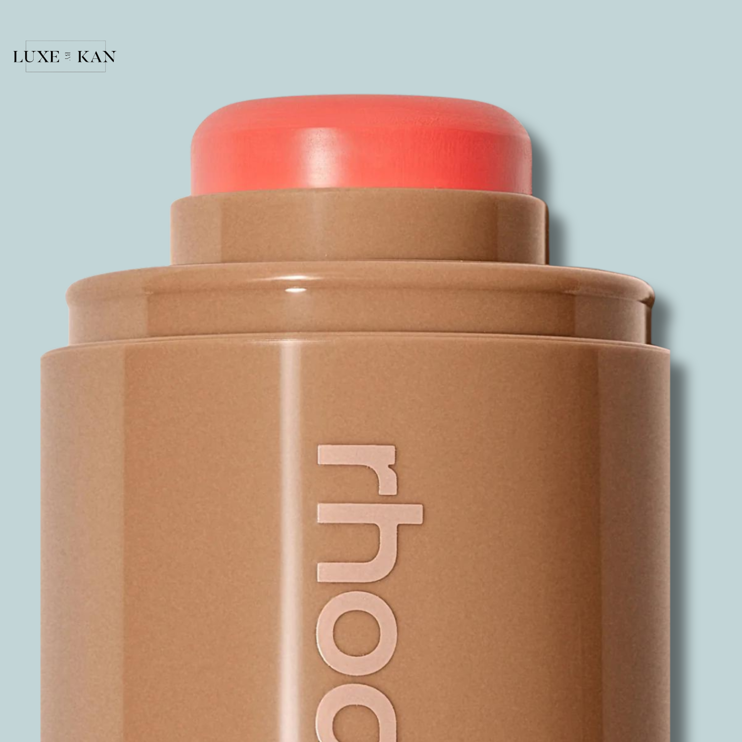 Close-up of a skin tone makeup stick with a coral-colored cap, featuring "rhodia" embossed on its brown packaging.