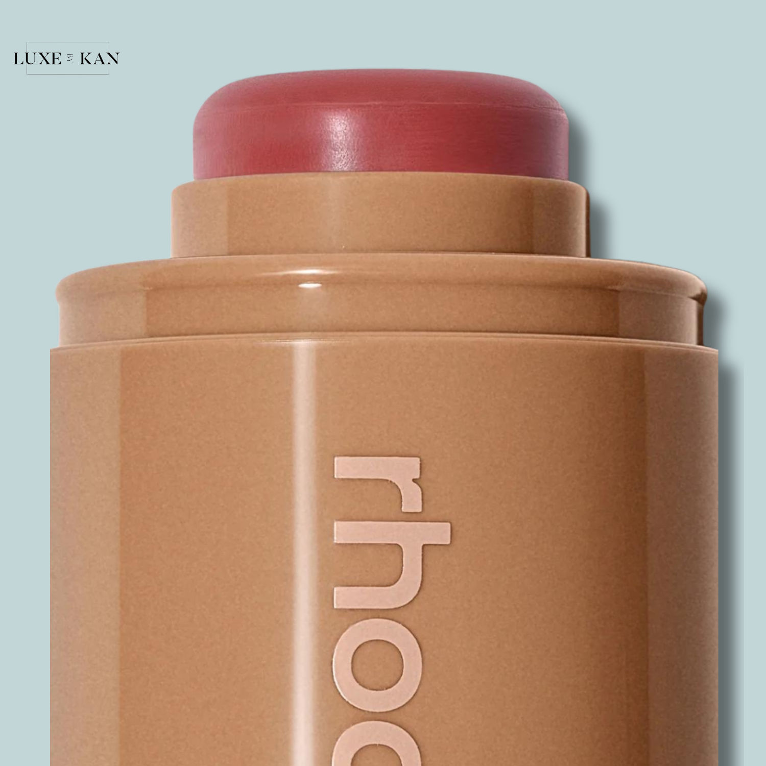 Close-up of a creamy blush stick in a sleek tan tube, featuring a rosy pink top and embossed "rhode" branding.