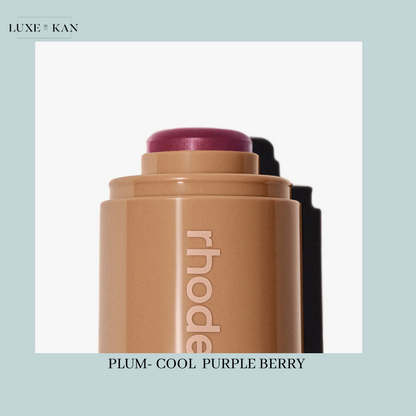 A close-up of a rhode makeup stick in a cool purple berry shade against a light blue background, showcasing its elegant design.