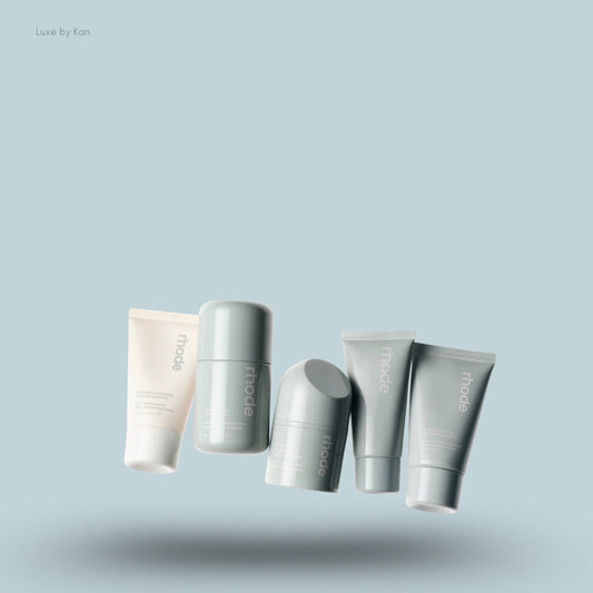 Five light-toned skincare products in various shapes and sizes from Rhode, featuring bottles labeled 'rhode'."