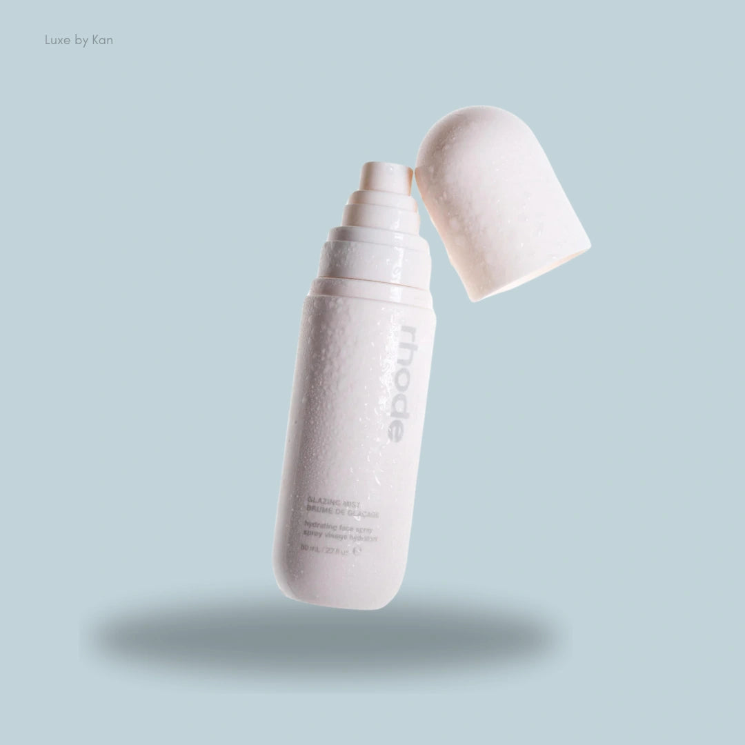A white spray bottle labeled "Rhode Glazing Mist," with its cap slightly open and water droplets on the surface, highlighting its fresh and dewy appeal.