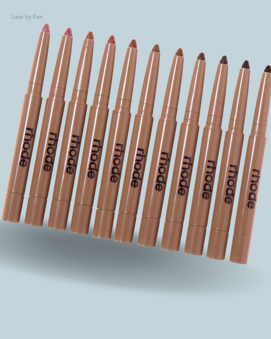 A row of twelve peptide lip-shaped crayon sticks from Rhode, showcasing a gradient of colors from light pink to deep brown.