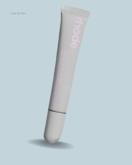 A gray tube of rhode Peptide Lip Treatment Balm against a soft blue background, featuring pink text highlighting the product's benefits.