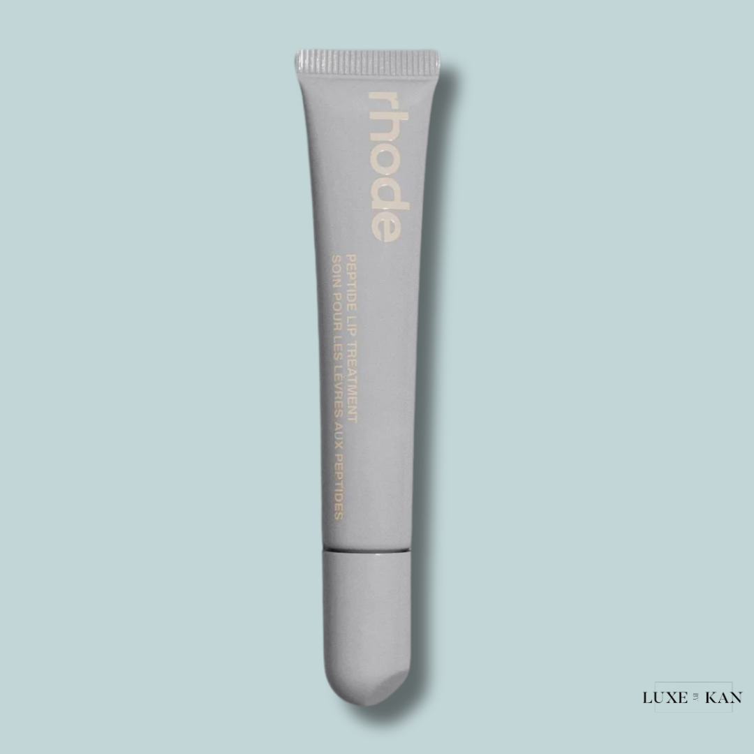 A gray tube of rhode Peptide Lip Treatment against a light blue background, labeled in elegant gold text.