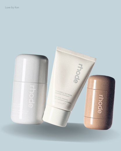Three skincare products from Rhode: a gray cleansing stick, a white daily cleanser tube, and a nude stick.