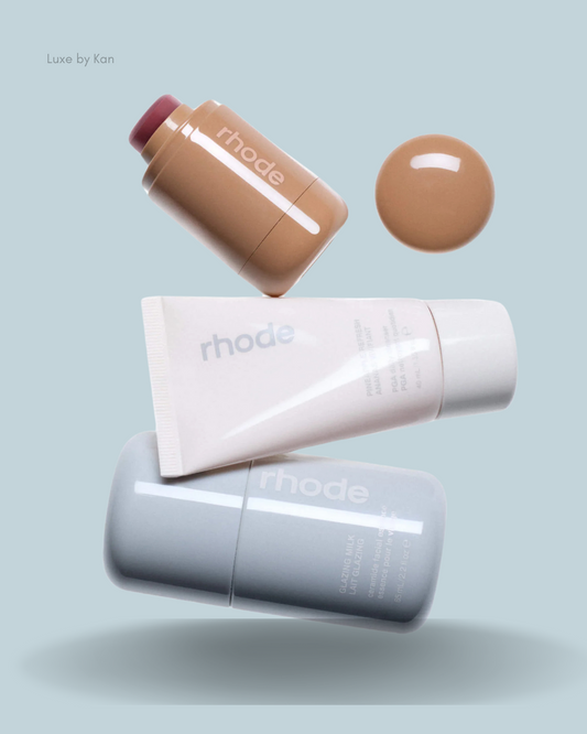 Three rhode skincare products displayed against a light blue background: a blush stick, a cream tube, and a liquid glaze.