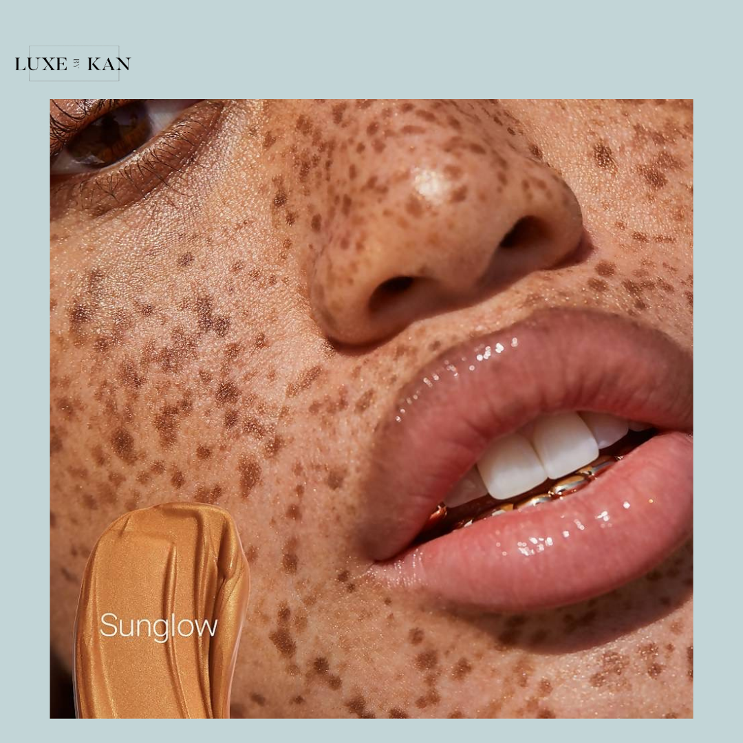Close-up of a model's freckled face wearing Saie Glowy Super Gel in Sunglow, showing radiant, dewy skin and glossy lips.