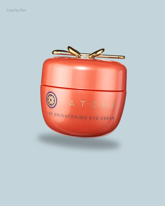 A coral Tatcha eye cream jar with a golden lid, labeled "The Brightening Eye Cream".