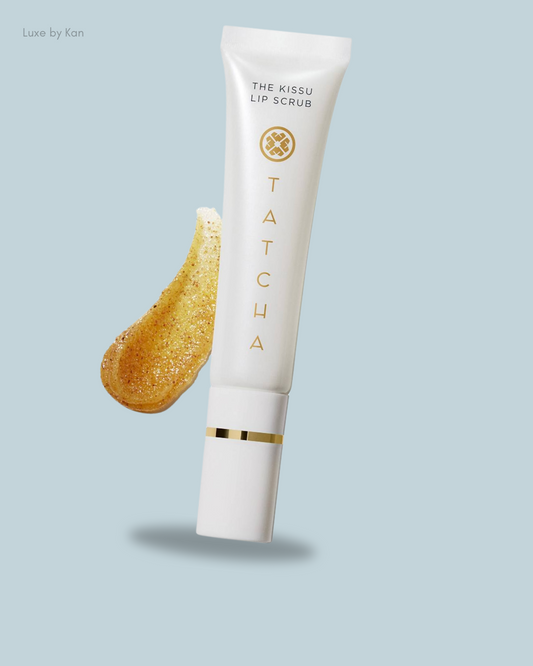 Tatcha's Kissu Lip Scrub tube and a dollop of golden scrub against a soft blue background, showcasing smooth, exfoliating lip care.