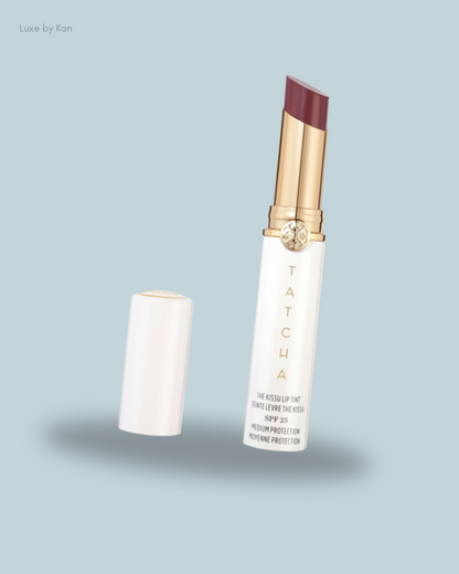 A Tatcha Kissu Lip Tint with SPF 25 in a sleek white tube, partially opened to reveal a rich plum shade.