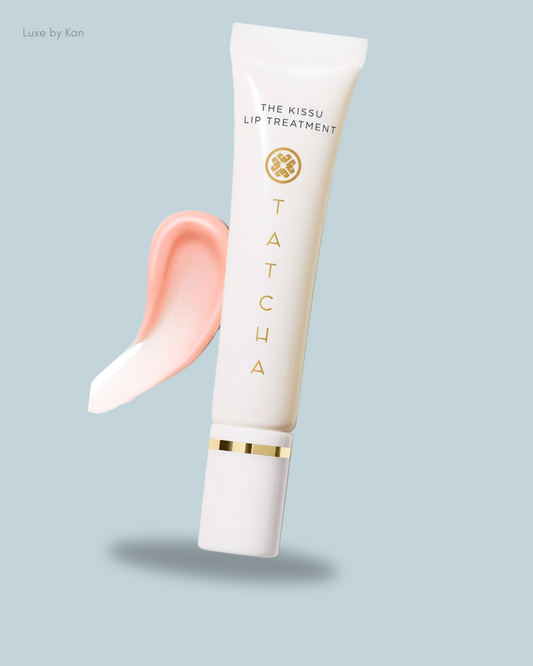 Tatcha's Kissu Lip Treatment tube with a pink lip balm swatch against a soft blue background, showcasing elegant skincare.