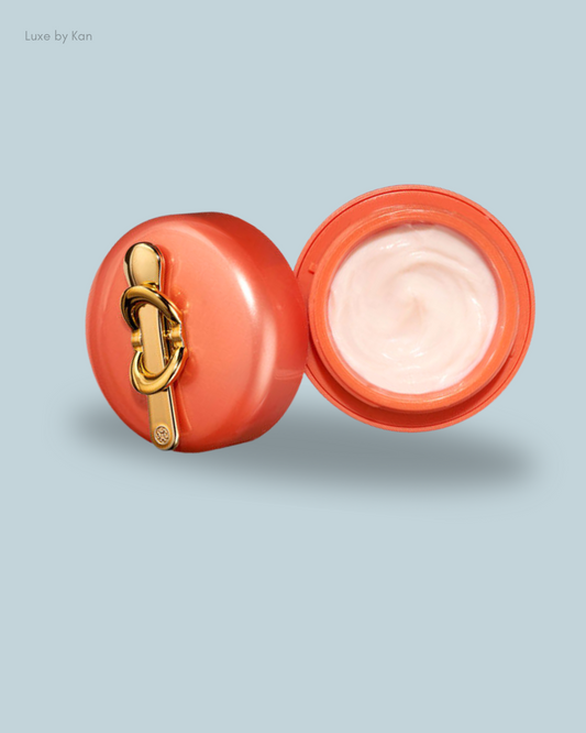 Open coral-colored cream container with a gold clasp, revealing smooth, glossy white cream inside.