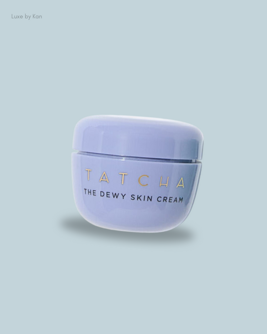 A lavender jar of Tatcha The Dewy Skin Cream with a gold logo on a light blue background, showcasing luxurious skincare.