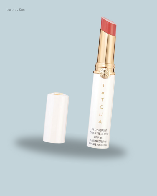 A Tatcha lip tint in a white tube with gold accents, featuring a pink balm and SPF 25.