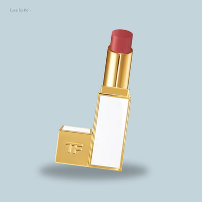 A luxurious gold lipstick with a soft pink shade, featuring a sleek design and a white label, set against a light blue background. 