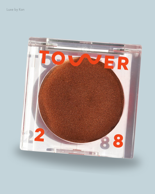 A clear makeup compact containing Bronzino Illuminating Cream Bronzer, labeled "TOWER 28."