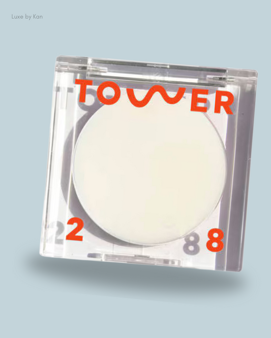 A clear compact of Tower28 SuperDew Highlighter Balm features a round white product inside, accented with bold orange lettering.
