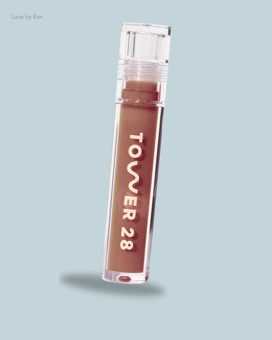 A clear tube of Tower 28 Beauty ShineOn Milky Lip Jelly in a warm brown shade.