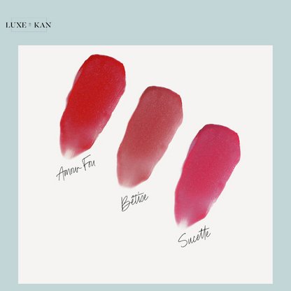Three vibrant lipstick swatches: a bold red "Amour Fou," a soft rosy pink "Bettie," and a bright fuchsia "Sucette" on a white background.