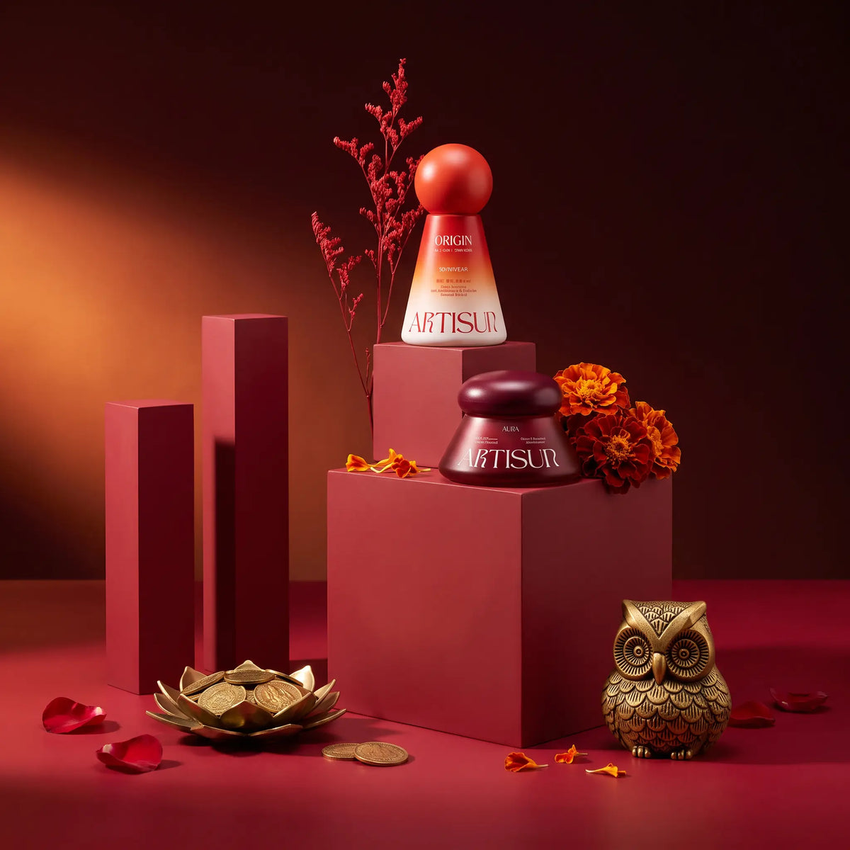 Artisun Origin and Aura sunscreens on red podiums with a brass owl, marigolds and gold coins