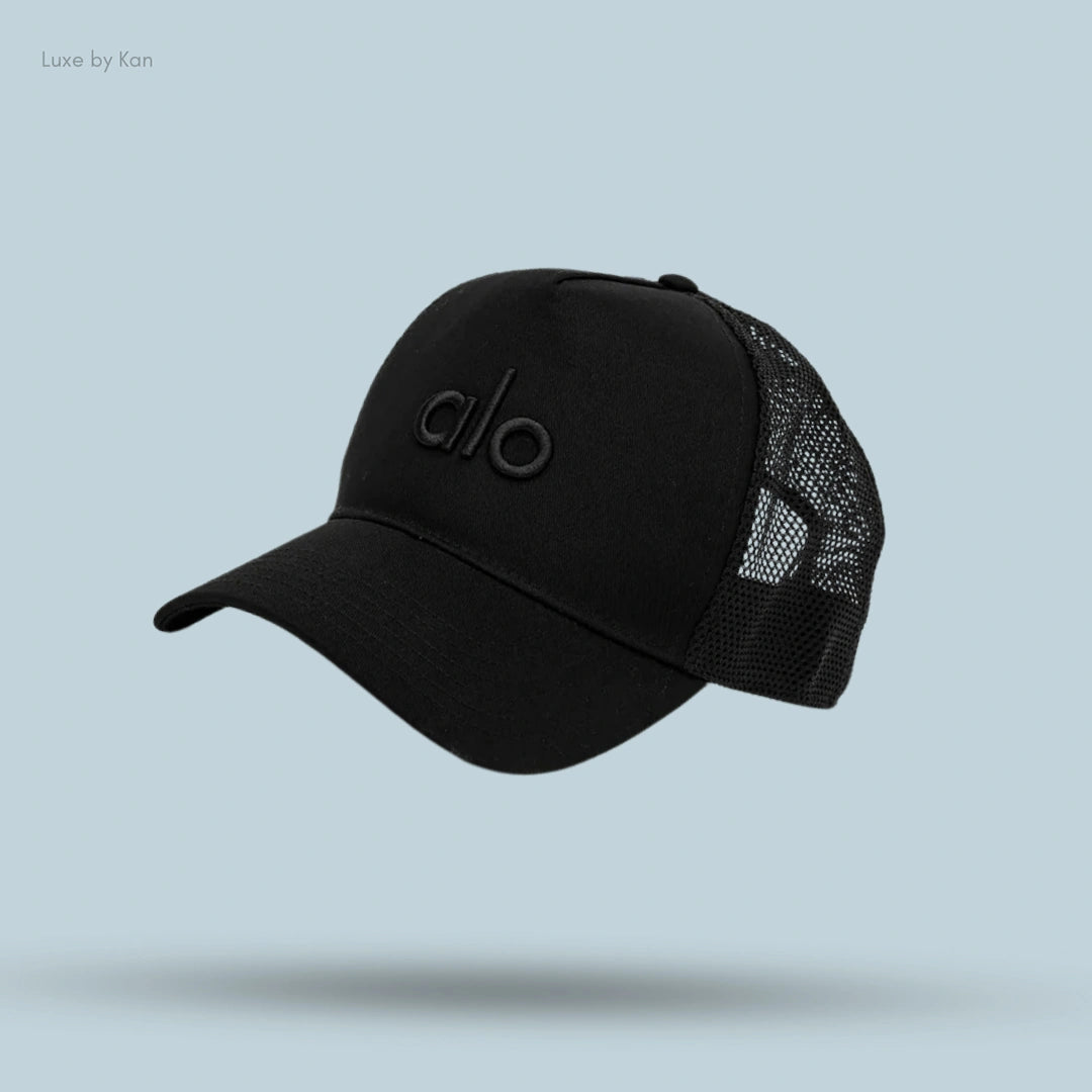 Alo District Trucker Hat in Black, flat lay on light blue background