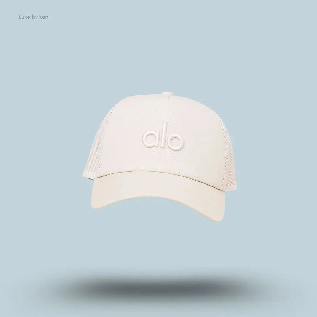 Alo District Trucker Hat in Bone, flat lay on light blue background
