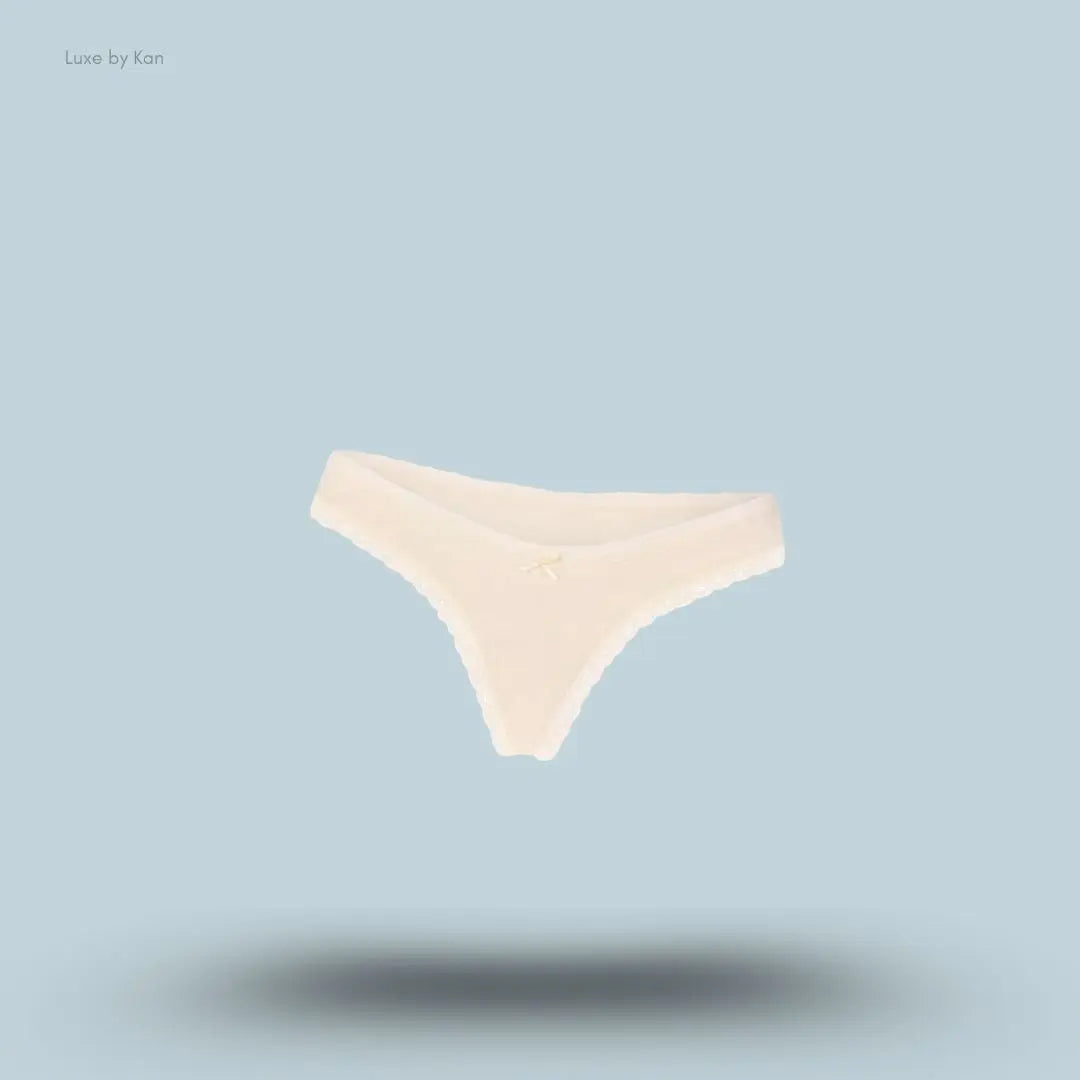 SKIMS Lightweight Cotton Lace Thong in Butter Tonal, flat lay on light blue background