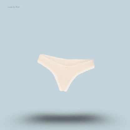 SKIMS Lightweight Cotton Lace Thong in Butter Tonal, flat lay on light blue background
