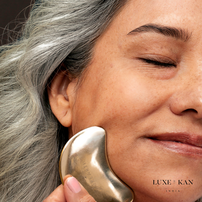 A woman with gray hair uses a Purearth kwansha facial beauty coin on her cheek, eyes closed, with the Luxe Kan India logo in the corner.