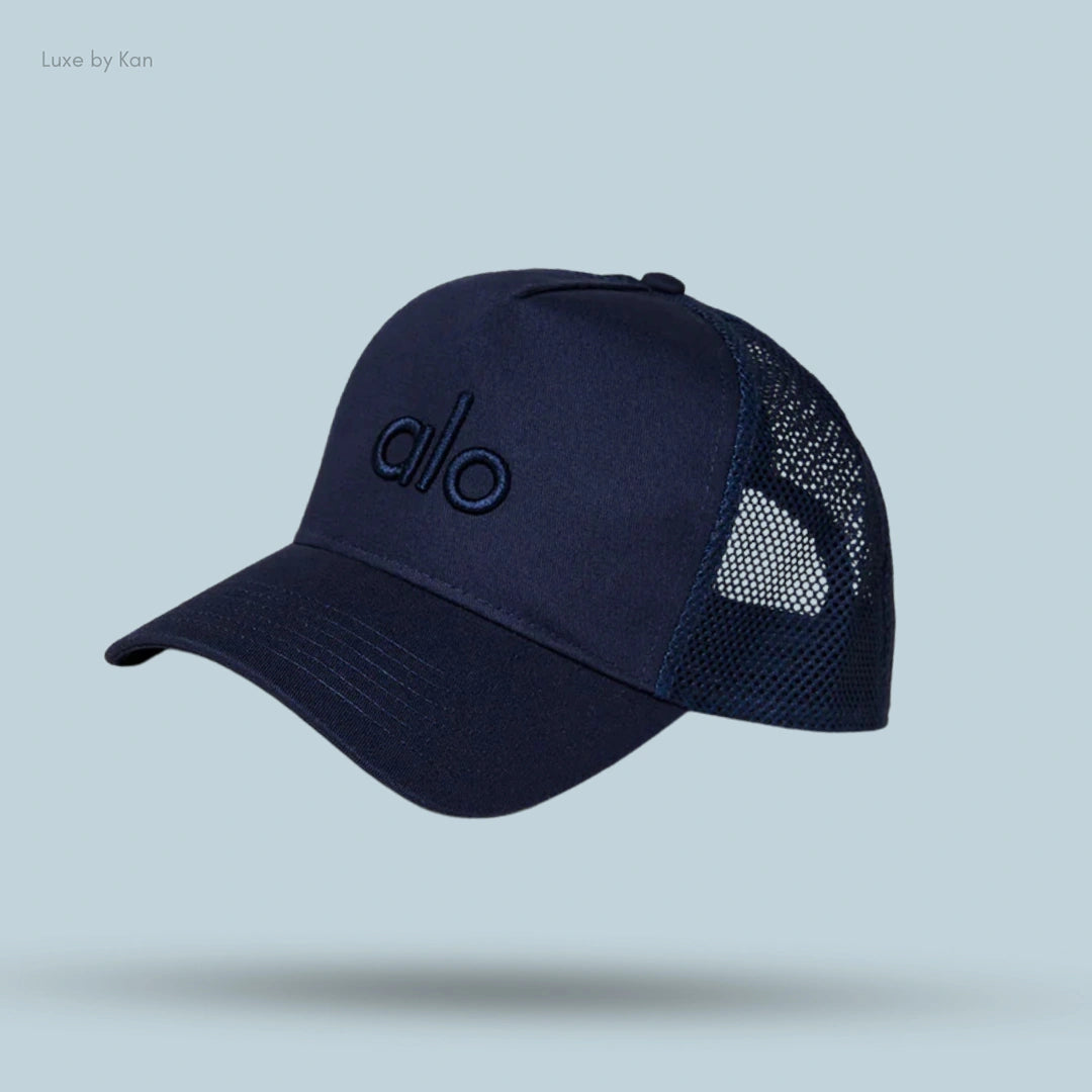 Alo District Trucker Hat in Navy, flat lay on light blue background