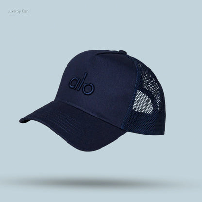 Alo District Trucker Hat in Navy, flat lay on light blue background
