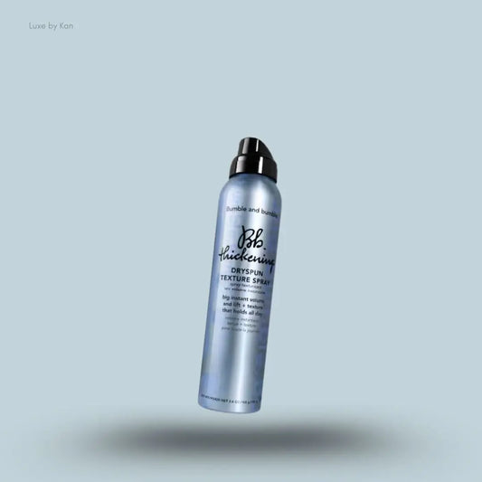 Bumble and bumble Thickening Dryspun Texture Spray aerosol can on a light blue background, angled product pack shot with shadow below