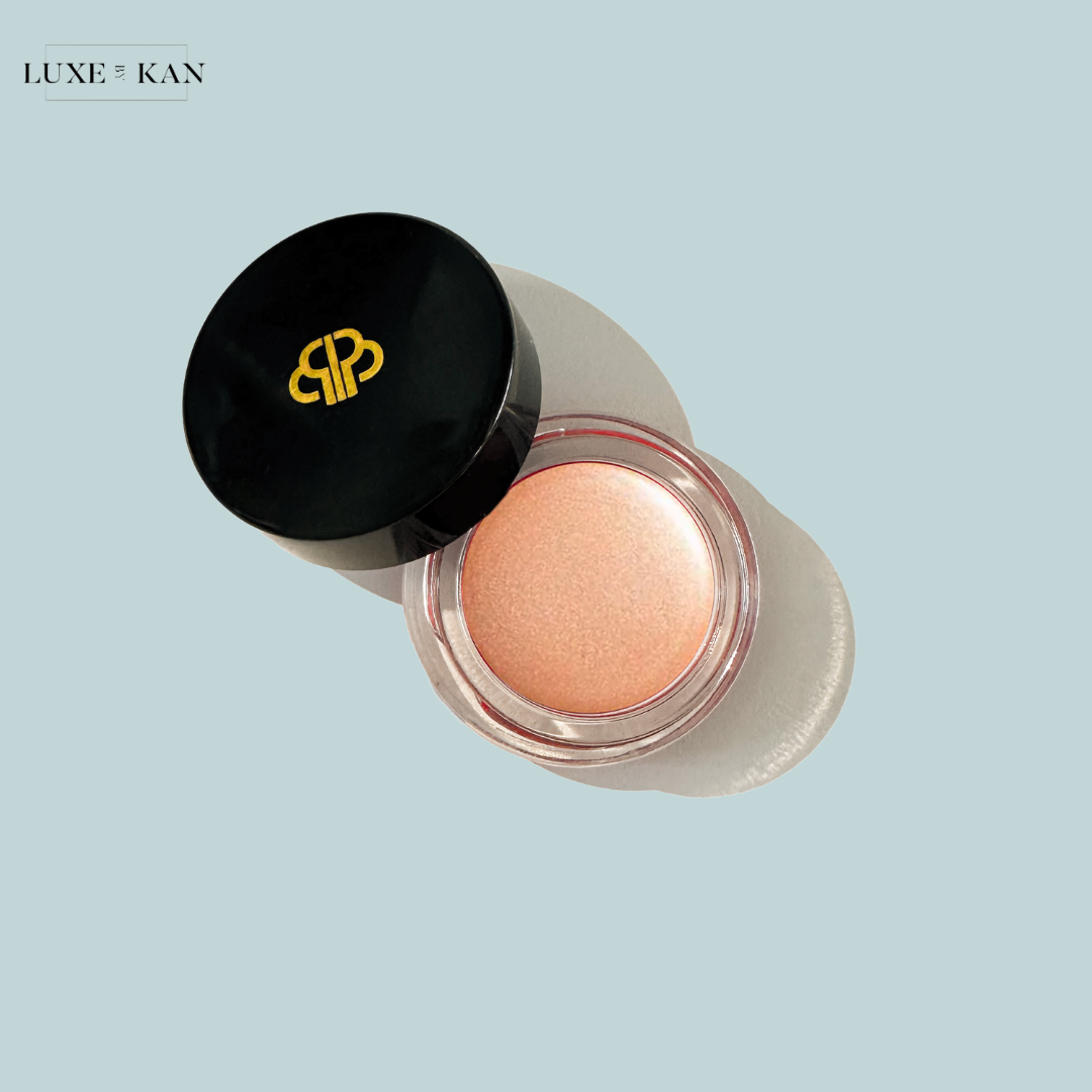 A shiny, peach-toned cream blush in a clear jar with a sleek black lid, featuring a gold logo of "Purearth sitara crème strobelighter".