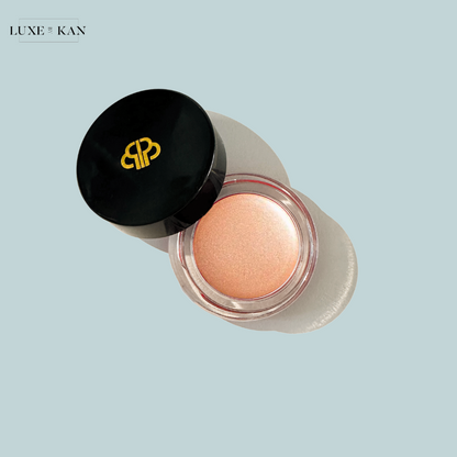 A shiny, peach-toned cream blush in a clear jar with a sleek black lid, featuring a gold logo of "Purearth sitara crème strobelighter".